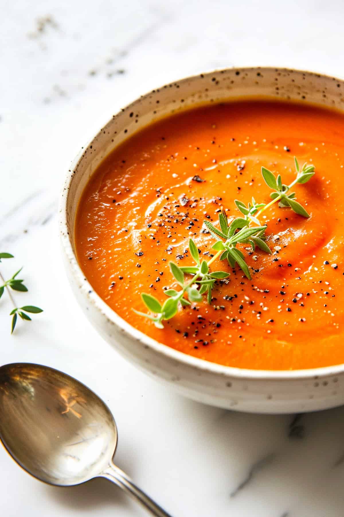 Roasted tomato soup in a bowl with thyme and olive oil.