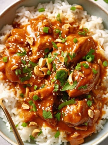 Peanut butter chicken in a white bowl with herbs and peanuts.
