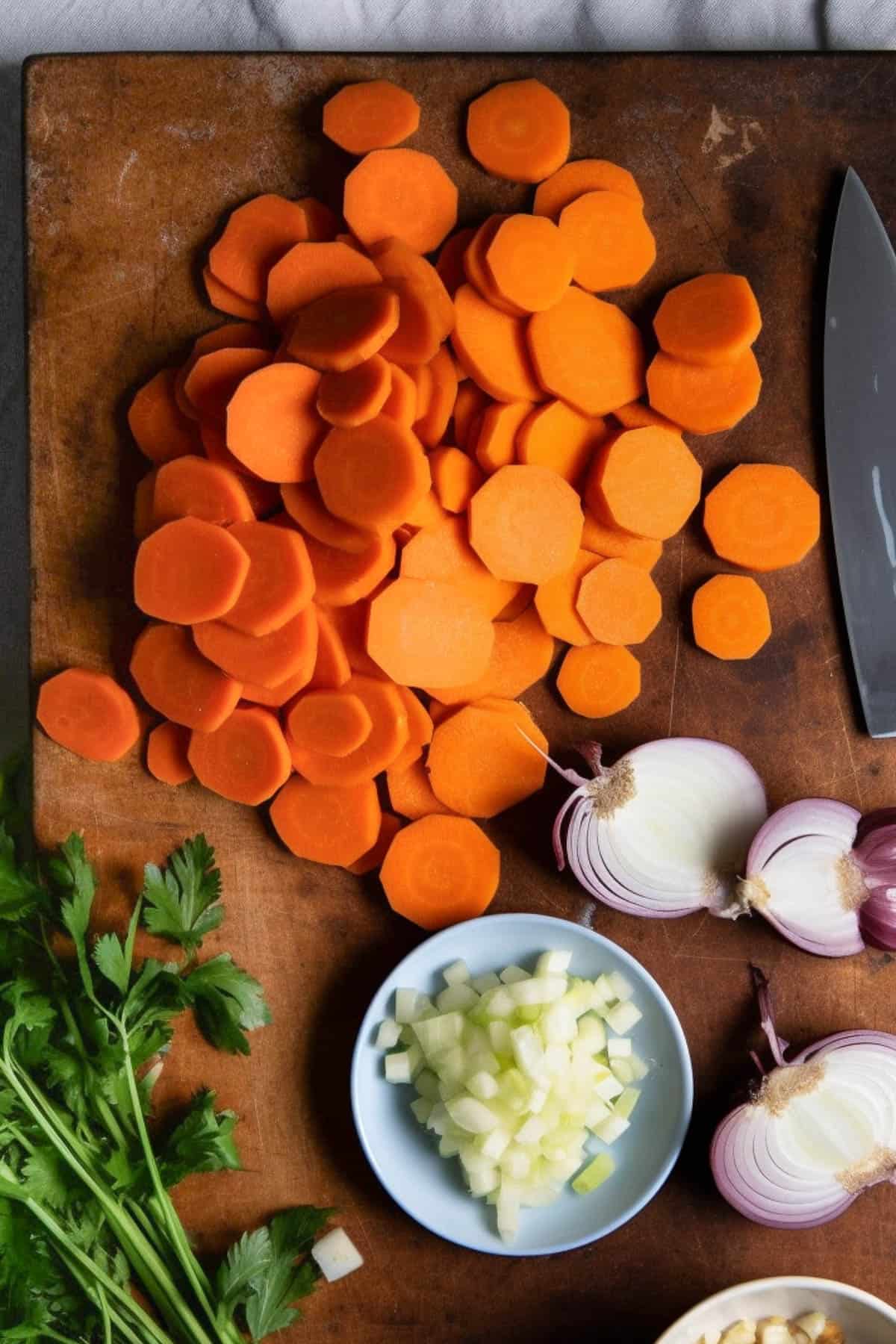 Carrots, onions and garlic on a chopping board to make soup.