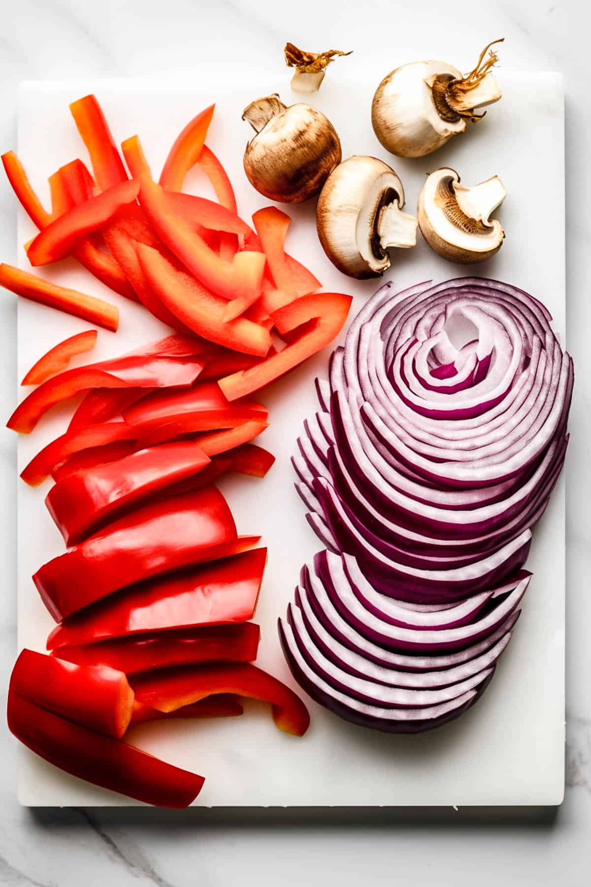 Sliced peppers, mushrooms and red onions on a white board for sausage casserole.