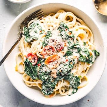 Creamy kale pasta with pine nuts and tomatoes in a white bowl.