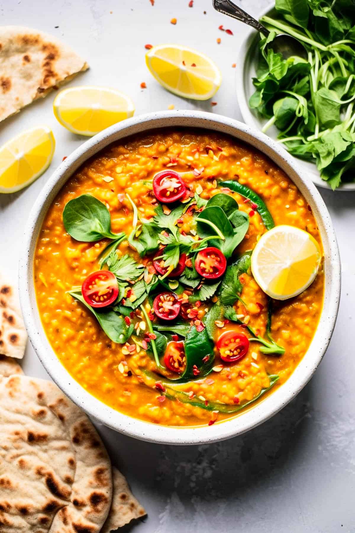Red lentil dhal with tomatoes and spinach in a bowl with lemon.