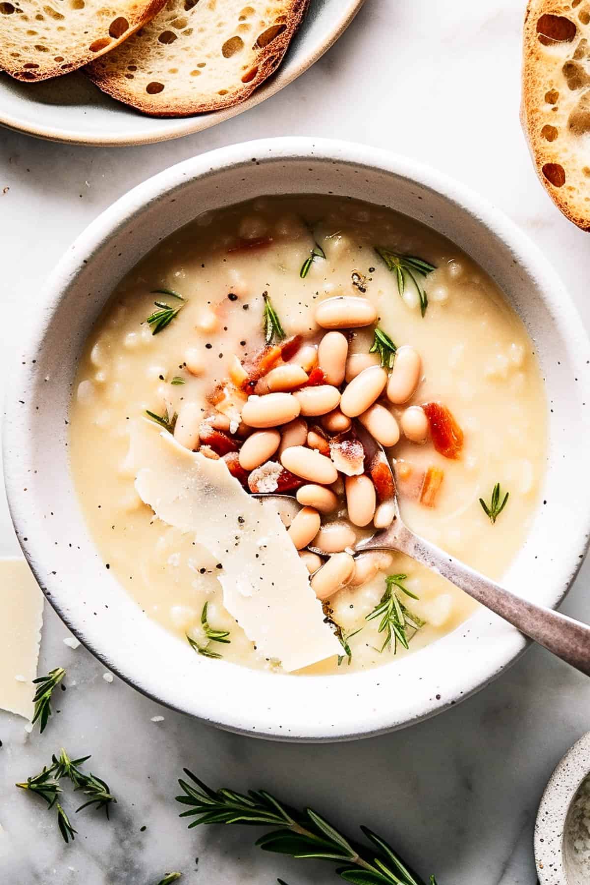 White bean soup with bacon and rosemary in a white bowl.