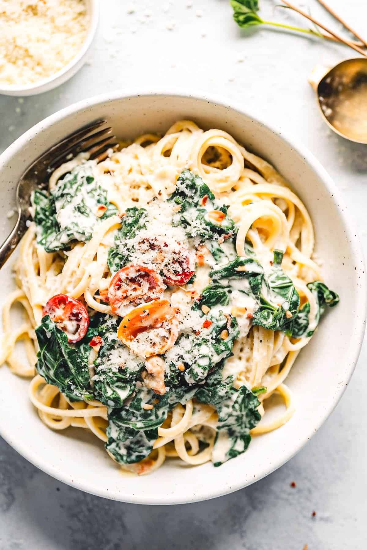 Creamy kale pasta with pine nuts and tomatoes in a white bowl.