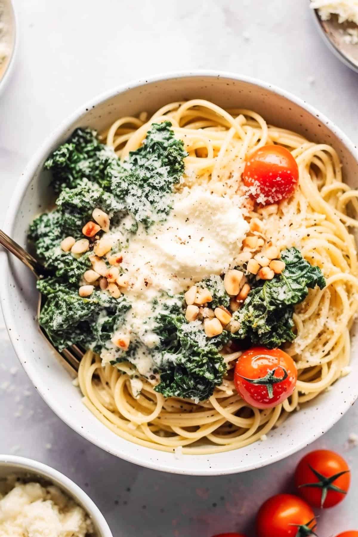 Creamy kale pasta with pine nuts and tomatoes in a white bowl.
