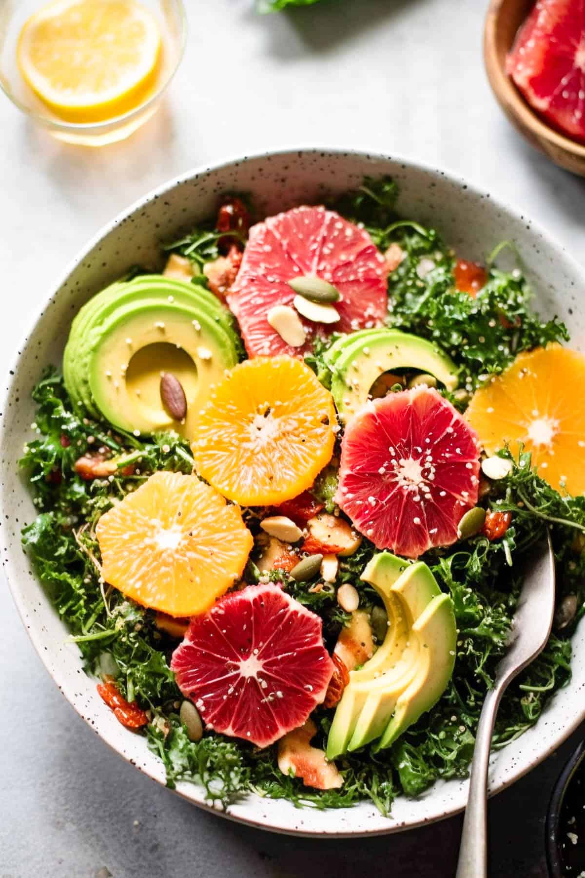Kale citrus salad with oranges and avocado in a bowl with nuts and seeds.
