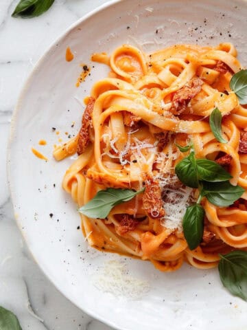 Sun-dried tomato pasta in a bowl with chopped basil and parmesan cheese.