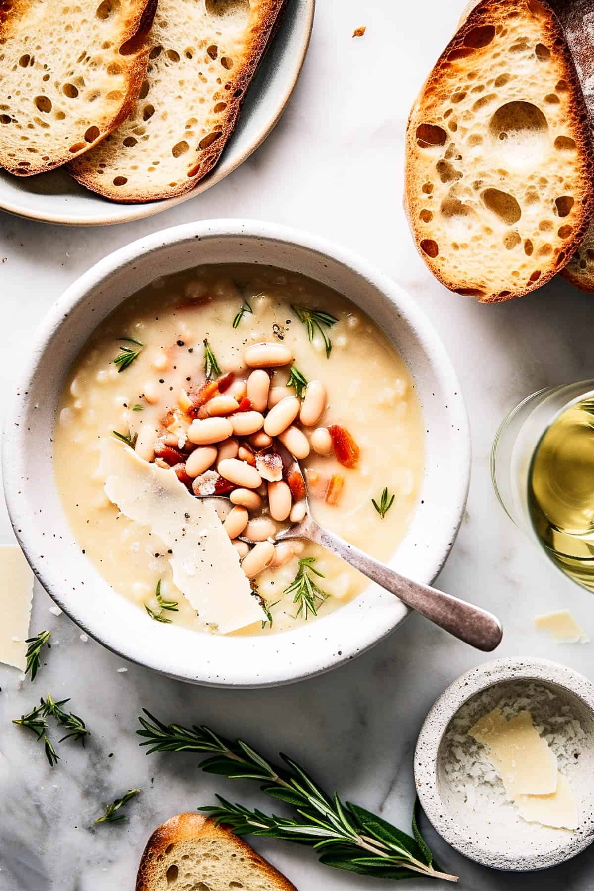 White bean soup with bacon and rosemary in a white bowl.