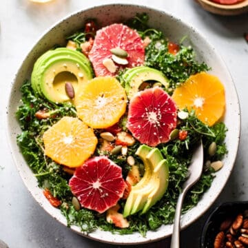 Kale citrus salad with oranges and avocado in a bowl with nuts and seeds.