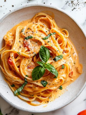 Creamy tomato pasta with basil and cheese in a white bowl.