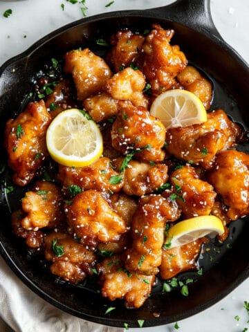 Sticky Chinese lemon chicken in a pan with lemon slices.