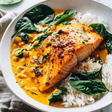 Coconut salmon curry in a creamy curry sauce on a white plate with spinach and rice.