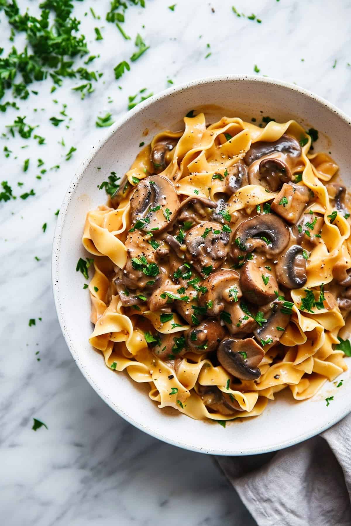 Creamy mushroom stroganoff with parsley and noodles in a white bowl.