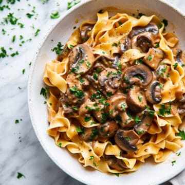 Creamy mushroom stroganoff with parsley and noodles in a white bowl.