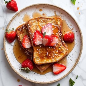Eggy bread with maple syrup and strawberries on a white plate.