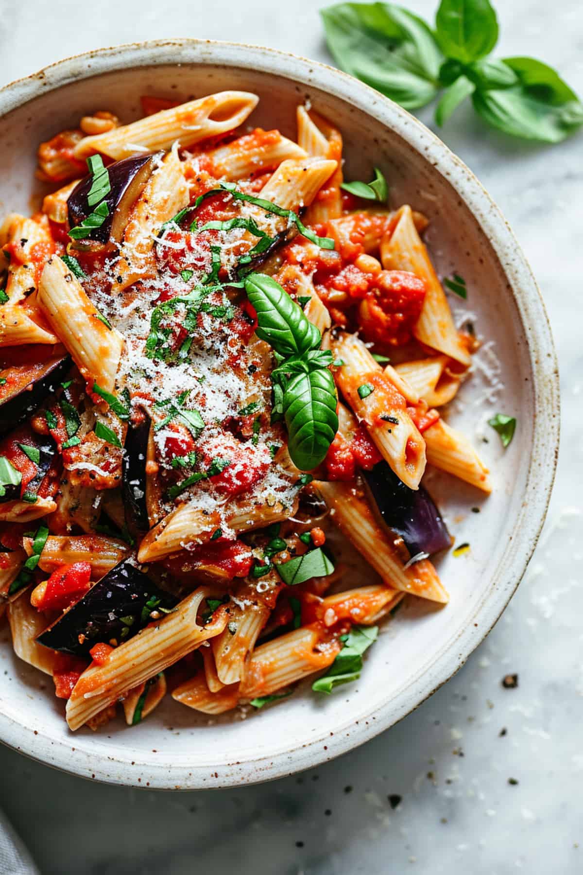 Easy aubergine pasta with parmesan and basil in a white bowl.