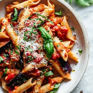 Easy aubergine pasta with parmesan and basil in a white bowl.