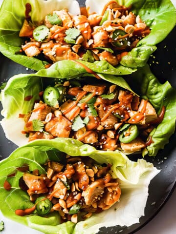 Asian chicken lettuce wraps in crisp lettuce cups with peanut sauce drizzled over top.