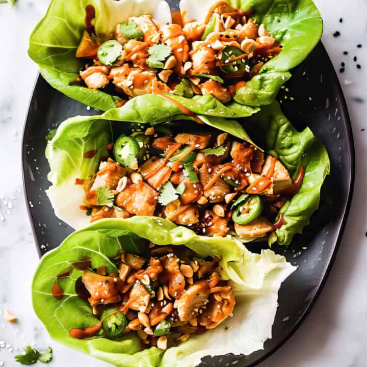 Asian chicken lettuce wraps in crisp lettuce cups with peanut sauce drizzled over top.
