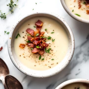 Bacon leek and potato soup with bacon bits and parsley in a white bowl.
