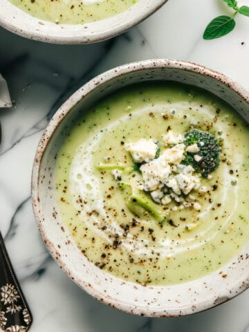 Bowls of creamy broccoli and stilton soup with crumbled blue cheese and black pepper on top.
