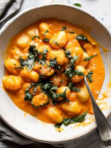 Butternut squash gnocchi with chopped herbs in a white bowl.