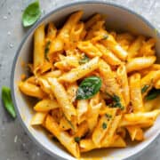 Butternut squash pasta sauce with penne pasta topped with parmesan in a white bowl.