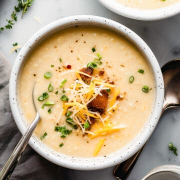 Cauliflower cheese soup with green onions and croutons in a white bowl.