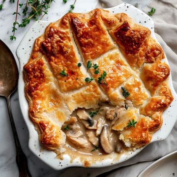 Chicken and mushroom pie with a puff pastry lid in a pie dish sprinkled with parsley.