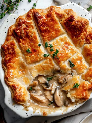 Chicken and mushroom pie with a puff pastry lid in a pie dish sprinkled with parsley.