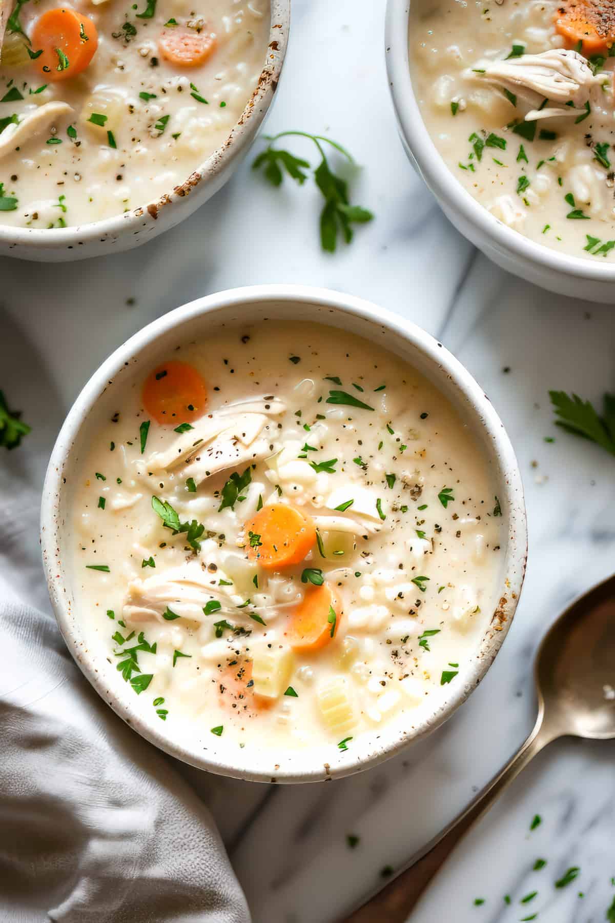 Easy creamy chicken and rice soup with parsley and carrots in a white bowl.
