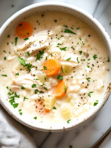 Easy creamy chicken and rice soup with parsley and carrots in a white bowl.