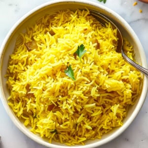 Pilau rice in a white bowl with a spoon.