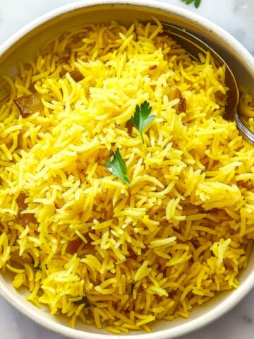 Pilau rice in a white bowl with a spoon.