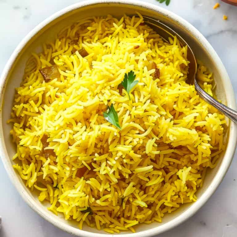Pilau rice in a white bowl with a spoon.