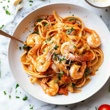 Prawn tomato pasta with basil and parmesan cheese in a white bowl.