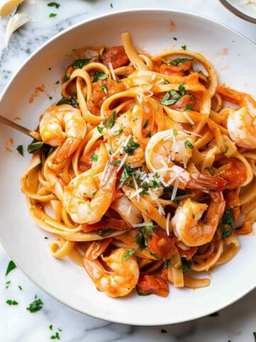 Prawn tomato pasta with basil and parmesan cheese in a white bowl.