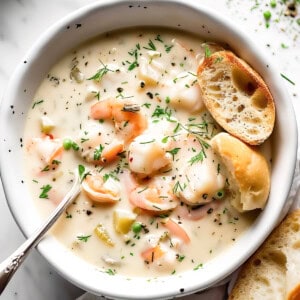 Creamy seafood chowder with salmon and prawns in a white bowl.