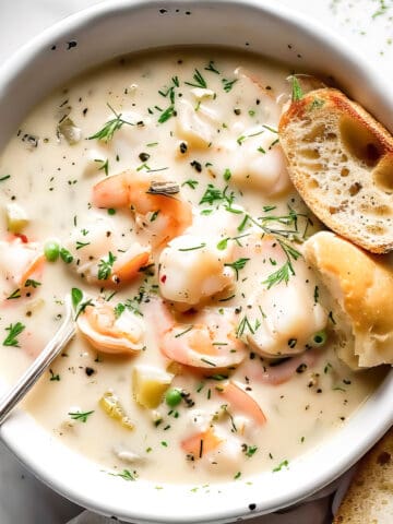 Creamy seafood chowder with salmon and prawns in a white bowl.