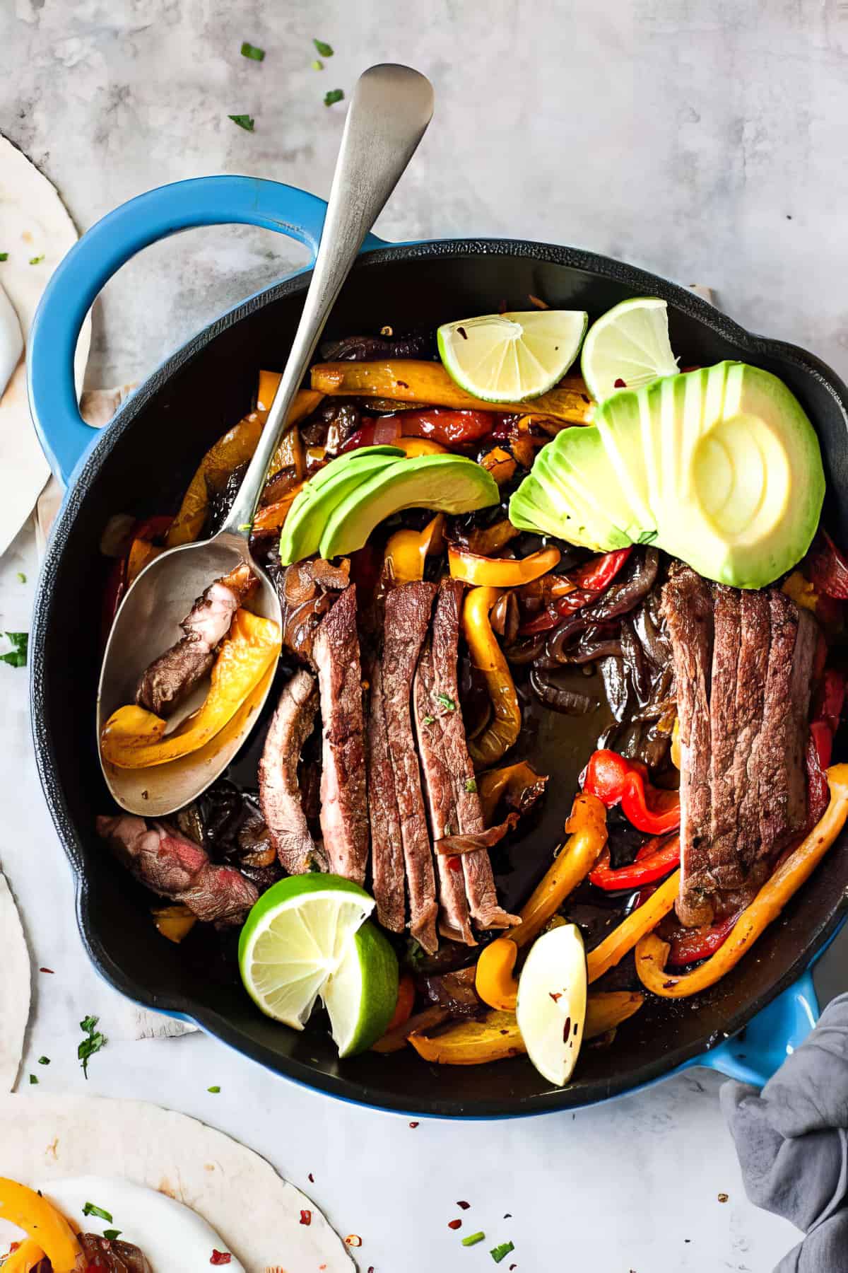 Steak fajitas with peppers and avocado in a skillet.