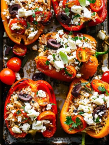Stuffed peppers with rice and tomatoes topped with feta and herbs on a baking tray.