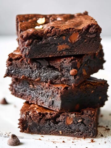 Triple chocolate brownies with cocoa powder on a white table.