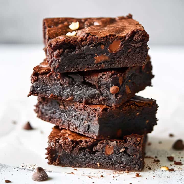 Triple chocolate brownies with cocoa powder on a white table.