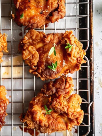 Crispy buttermilk chicken on a cooling rack with sea salt and thyme leaves.