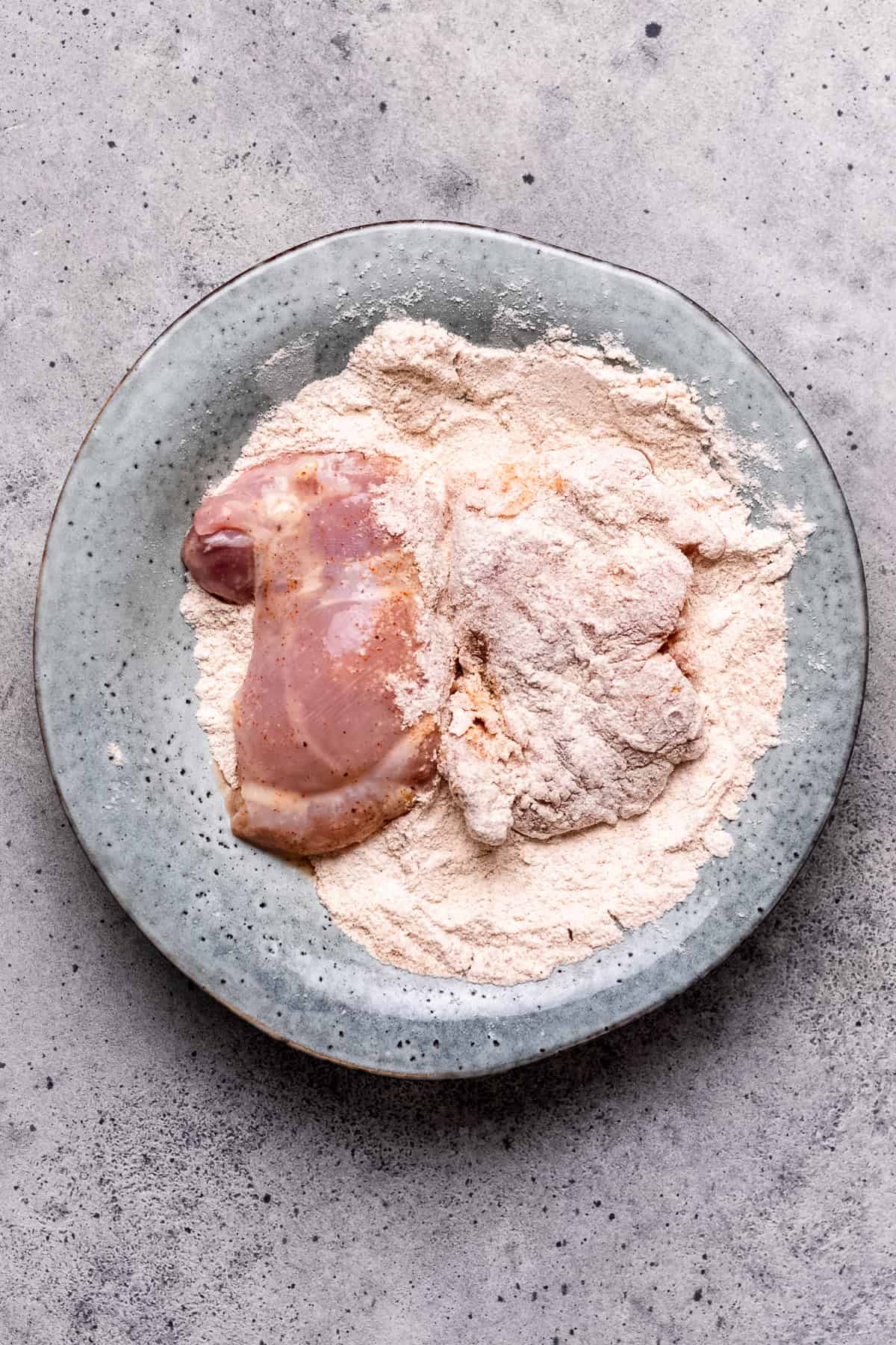 Chicken being tossed with flour for a crispy crust.