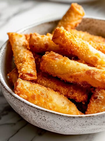 Crispy fried homemade egg rolls in a white bowl.