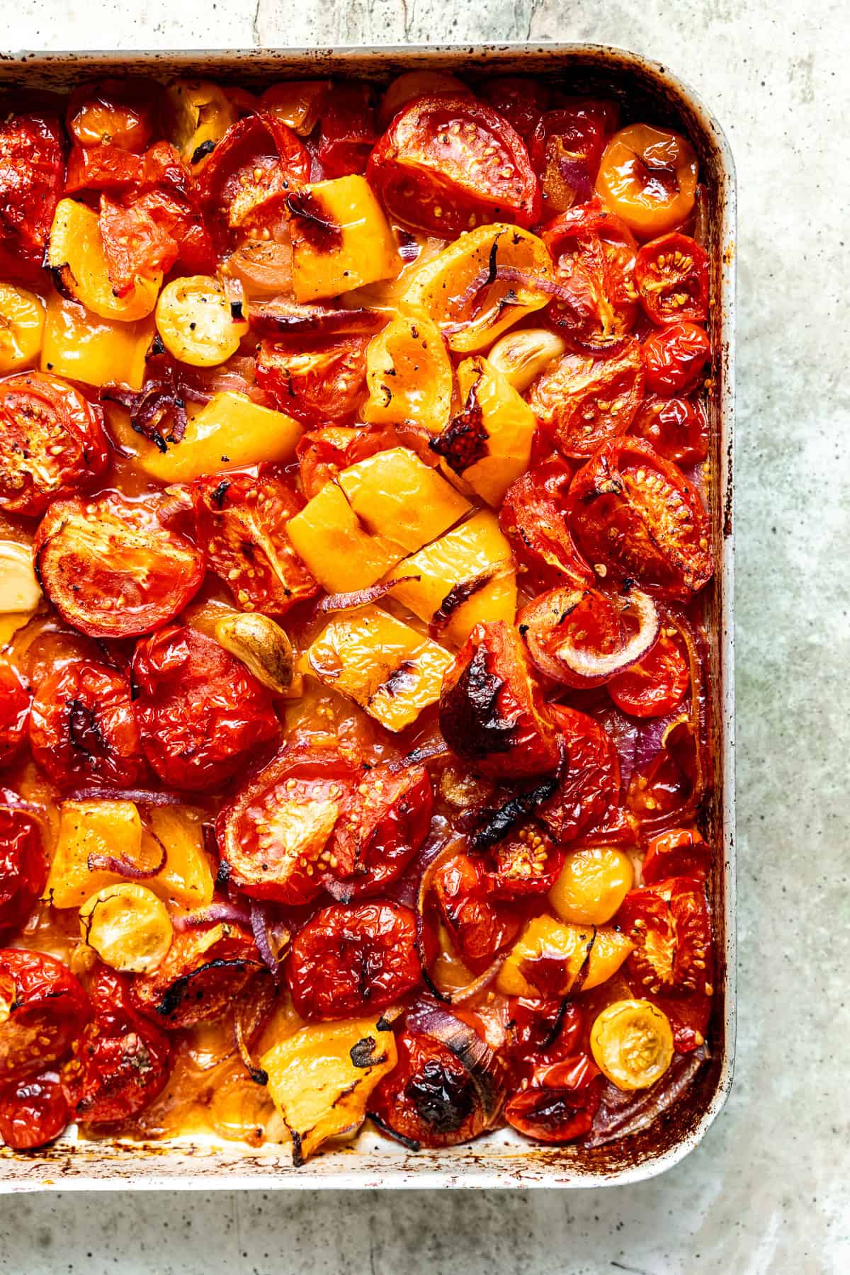 Roasted tomatoes with onions and garlic in a pan on a counter top.