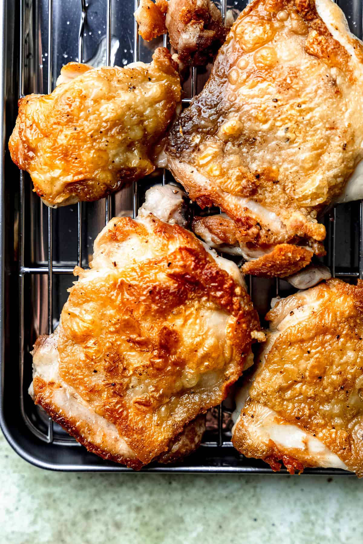 Crispy chicken thighs on a cooling rack.