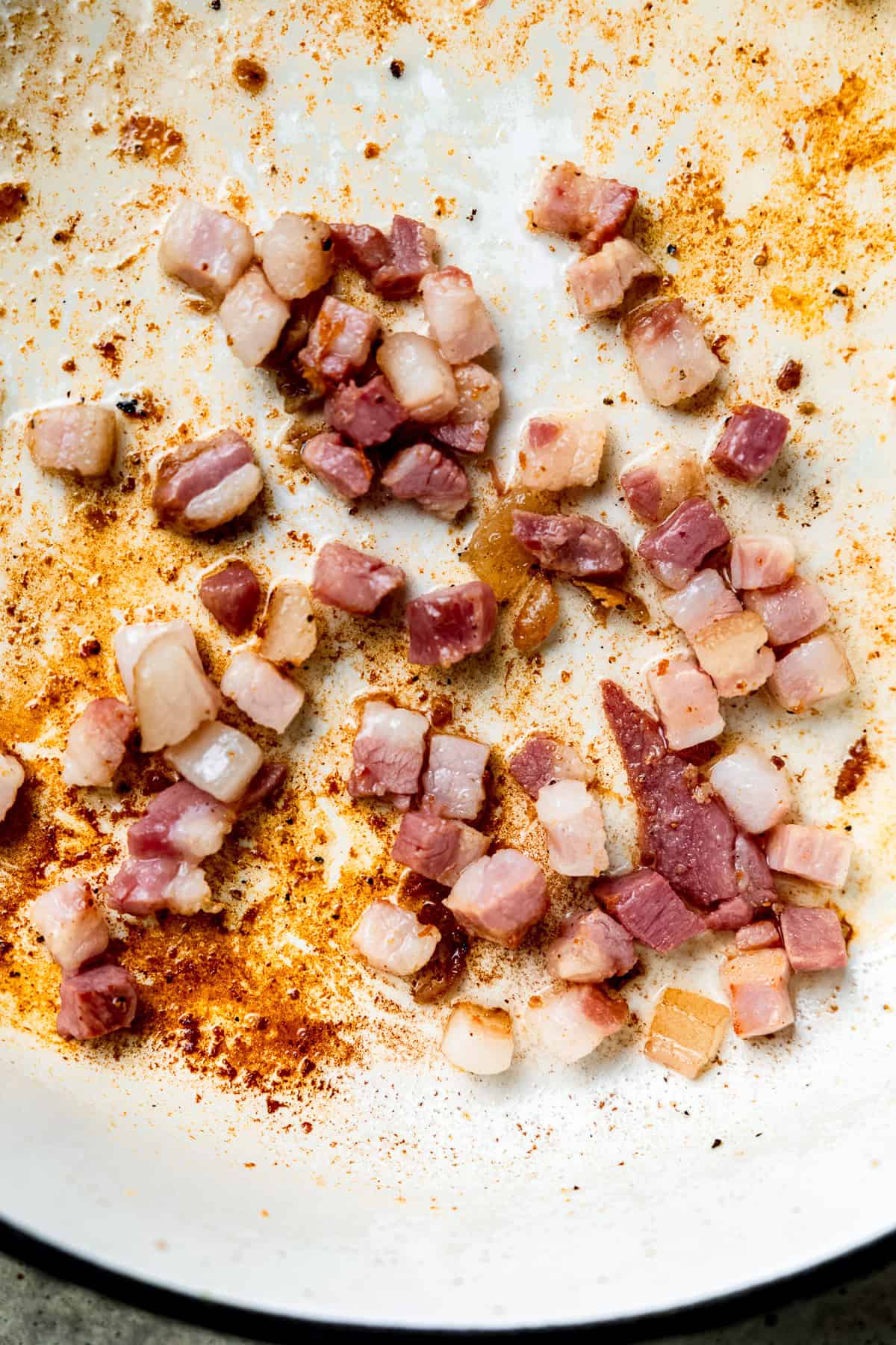 Bacon being cooked in a pan until crispy.